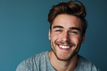 A man with a beard is smiling in front of a blue background