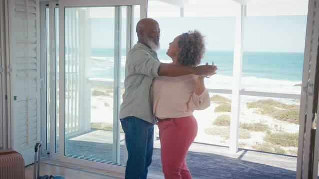 Mature couple with luggage arriving for holiday in beach front property overlooking ocean dancing together - shot in slow motion