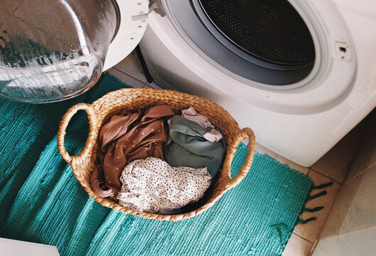  A basket with laundry by a washing machine.