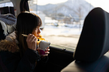 Young Asian woman sitting on car backseat and eating hot cup noodles meal during travel on car in...