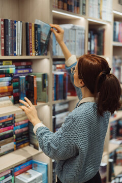 A focused woman in glasses selecting a book from library shelves.