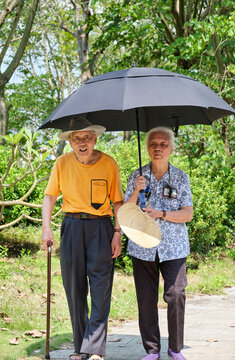 Chinese elderly couple walking in the park holding umbrellas