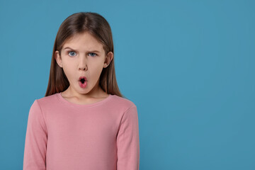 Portrait of surprised girl on light blue background. Space for text