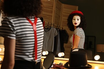 Young woman in mime costume posing near mirror indoors