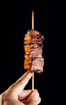 Crop person holding bacon skewer grilled in robata