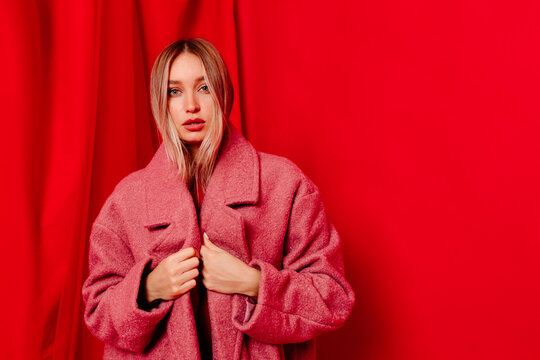 Young woman standing in oversized coat near red curtain