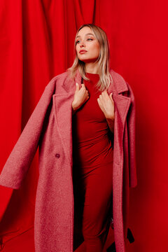 Stylish woman in coat standing over red studio background