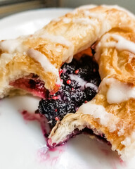 Close-up of a black raspberry danish pastry drizzled in a cream cheese icing on a white plate