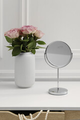 Mirror and vase with pink roses on white dressing table in makeup room