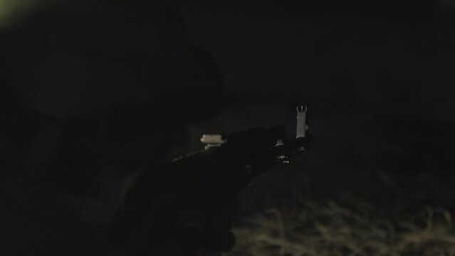 Soldier shoots at an enemy with a machine gun at night. Male soldier aims a machine gun at nigh. Night fight. Shooting from a machine gun on a dark background