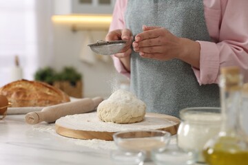 Making bread. Woman sifting flour onto dough at white table in kitchen, closeup
