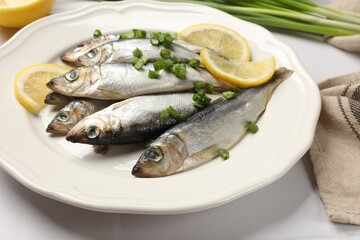 Fresh raw sprats, green onion and cut lemon on white table, closeup