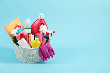 Different cleaning products in basket on light blue background, space for text