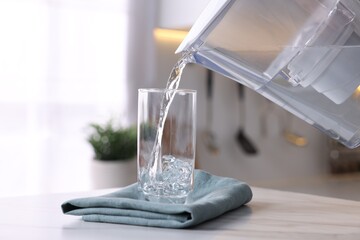 Pouring water from filter jug into glass in kitchen, closeup