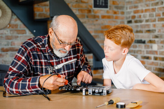Grandfather teaches grandson to use a soldering iron