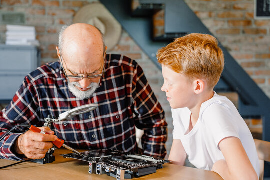 Grandfather teaches grandson to use a soldering iron