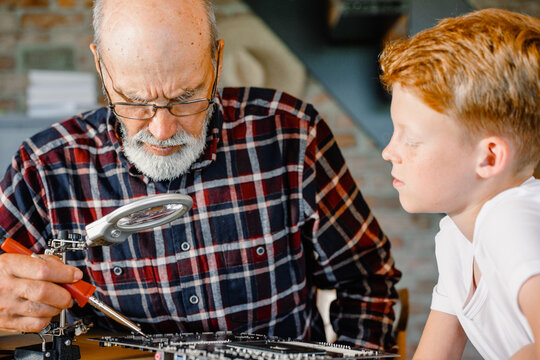 Grandfather teaches grandson to use a soldering iron