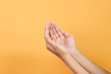 Hands showing praying hands gesture isolated on yellow background.