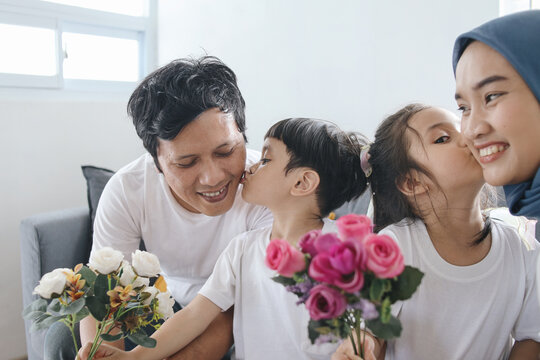 Kids Kissing Parents And Giving Flowers. Son Kiss Father and Daughter Kiss Mother at Home. Family Bonding.