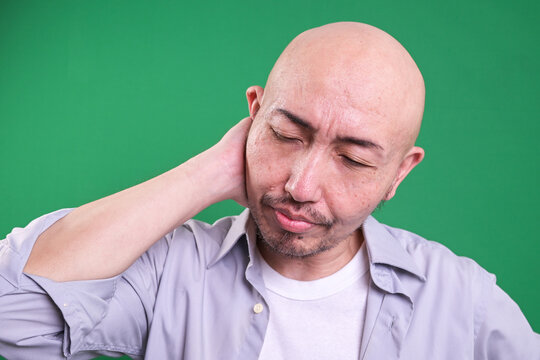 Unhappy fatigue man suffers from neck pain, closes eyes with dissatifaction. Exhausted office worker comes home tired isolated over green background.