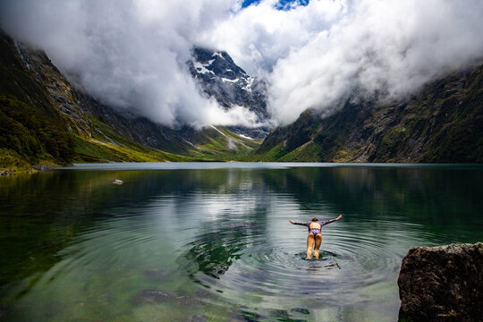 pretty girl in a swimsuit diving into famous alpine lake marian surrounded with mountains lake in fiordland national park near milford sound, new zealand, southland, south island