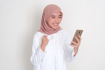 Moslem Asian woman clenched fist showing excitement when looking to her mobile phone