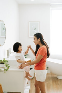 Asian little girl with mom brushing teeth in bathroom