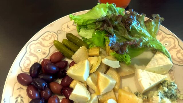 Assortment of different cheeses, salad and pickled vegetables. Antipasto appetizer plate. A plate of olives, cheese and salad.