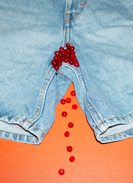 Conceptual photo of jeans and red pearls presenting period blood 