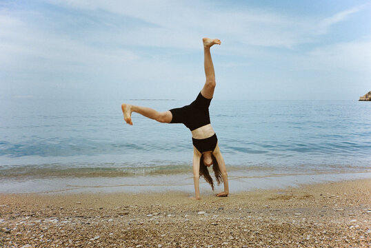 Young woman turning handsprings on a beach opposite the sea