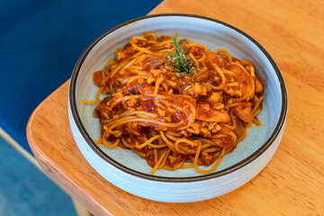 Spaghetti with tomato sauce on a plate on a wooden table ready to be served in a Thai restaurant.