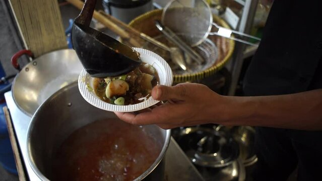 Putting beef soto sauce into a plastic bowl, Indonesian street food