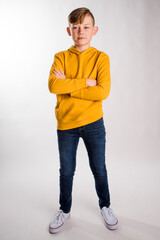  Cute smiling young boy in a yellow hoodie standing in a studio with arms crossed