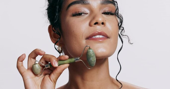 Woman, face and jade roller in studio for skin, dermatology and happy for self care by white background. Girl, person or model with pride for facial skincare, cosmetics and stone tools for massage