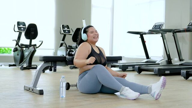 Portrait curvy girl drinking water after cardio exercise in fitness gym, plus-size women workout in sports club attention to lose weight training built a new strong body, healthy wellness lifestyle
