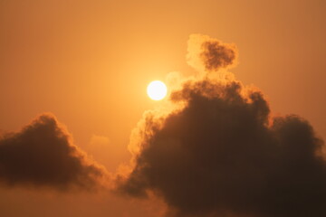 The sky is filled with clouds and the sun is shining brightly. The sun is the center of attention in the image, and it is surrounded by a few clouds. The sky has a warm and inviting atmosphere
