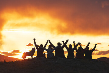 Big group of happy friends are sitting with open arms against sunset sky