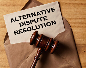 A gavel lies on top of an envelope on wooden background, which is open and contains a piece of paper that says word text Alternative Dispute Resolution acronym ADR
