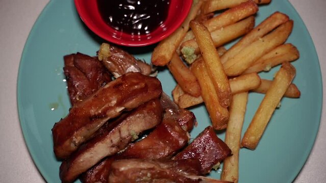 Pork ribs in a plate with fries and sauce.
