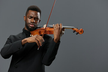 A talented black man in a stylish suit playing the violin with passion on a neutral gray background