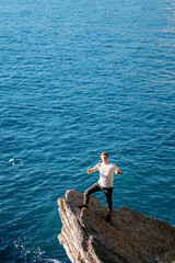 Fototapeta na wymiar Young smiling man standing on a stone ledge above the sea with his thumbs up