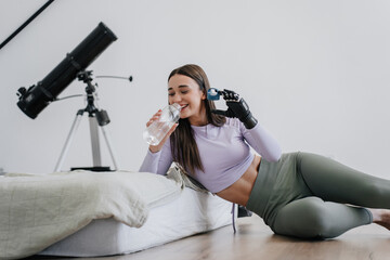 Woman with bionic hand drinking water, fitness glove, telescope background.