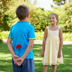 Obraz premium Children, smile and flower in park with surprise for crush, gift or friendship for spring and childhood on grass with tree. Little girl and boy with happiness and plant behind back for and joy