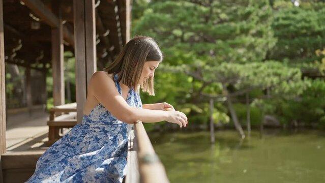 Captivating portrait of a beautiful hispanic woman enjoying nature's bounty, feeding fish by the tranquil heian jingu pond in kyoto's traditional shrine park