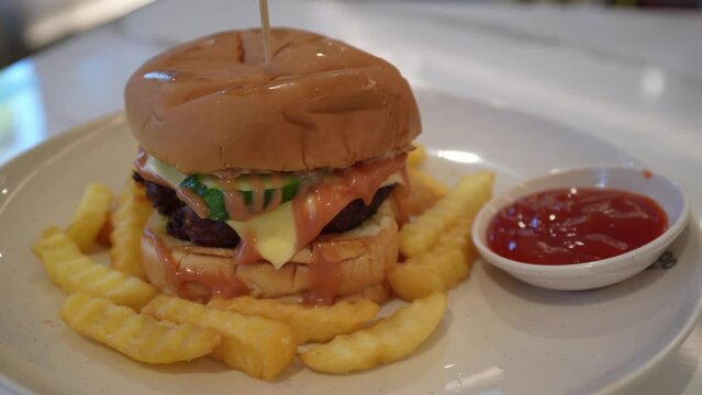 Close-up view of the delicious pork burger with cucumber, cheese, French fries with chili sauce.