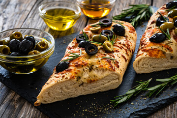 Focaccia alle olive - baked sandwich with green and black olives and rosemary on wooden background
