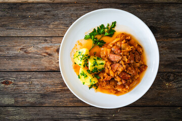 Bigos - cooked cabbage with sliced sausage and boiled potatoes on wooden table