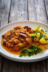 Bigos - cooked cabbage with sliced sausage and boiled potatoes on wooden table