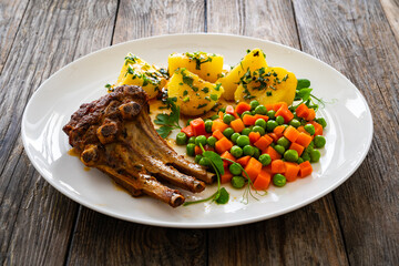 Veal ribs, boiled potatoes, peas and carrots on wooden table
