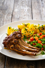 Veal ribs, boiled potatoes, peas and carrots on wooden table
